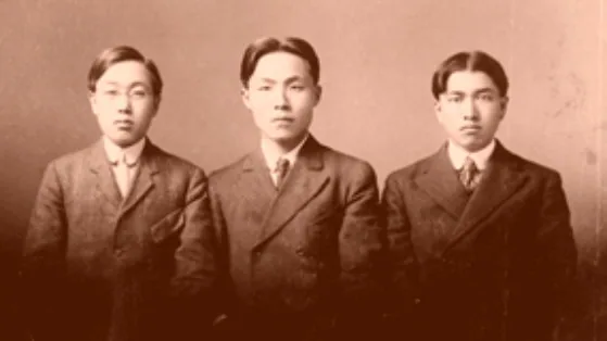 A sepia studio photograph of three young Korean men in dark suits and ties, Song Jong Ik, Dosan and Pang Hwajung, the man in the centre clean-shaven, San Francisco 1905