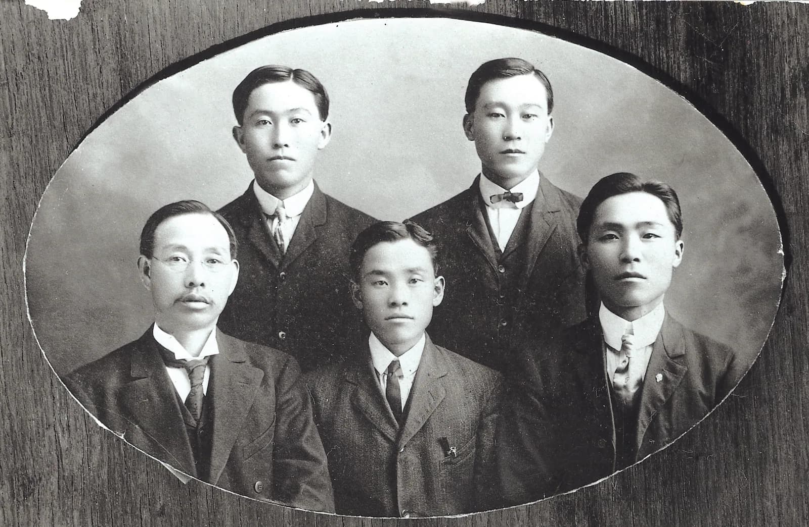 양복 차림 남자 다섯 명의 타원형 사진관 사진. 안경을 쓴 나이 든 남자 한 명이 앉아 있다
