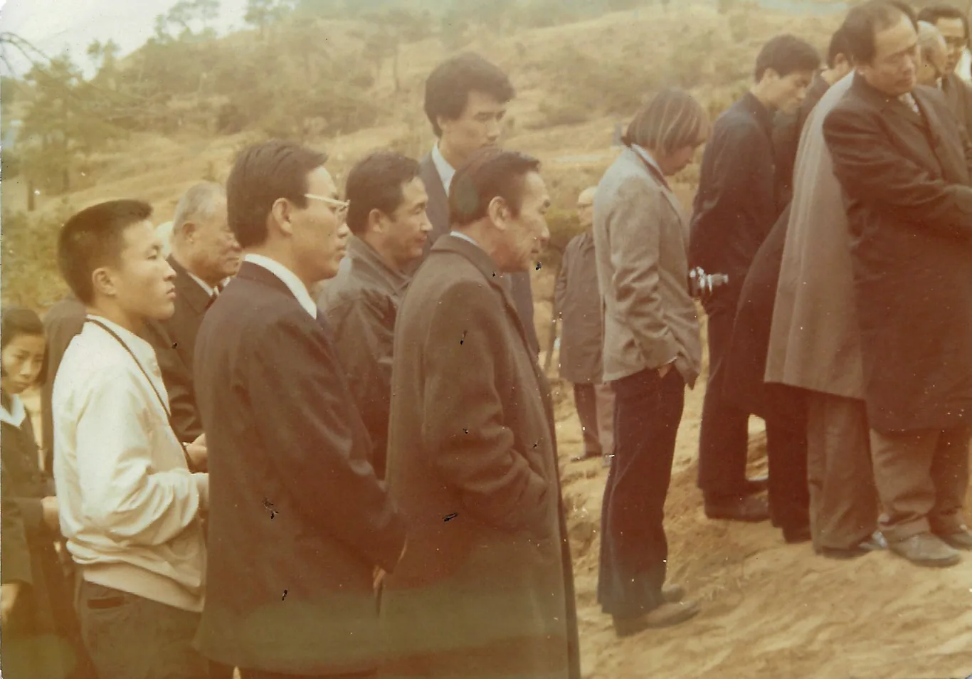 Two men at a graveside on a hillside at Manguri, one holding a camera, during the 1973 exhumation