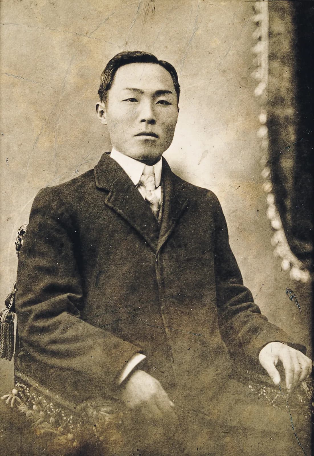 조각 장식이 있는 의자에 앉은 도산 안창호의 세피아 사진관 사진. 어두운 양복, 말끔히 면도한 얼굴, 1908년
